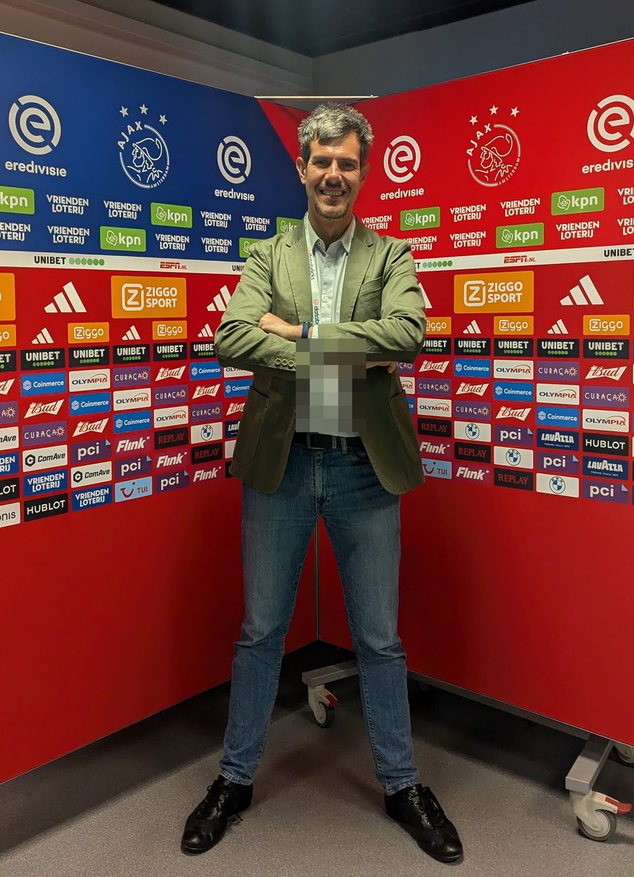 Luca Berton standing with arms crossed in front of the Ajax and Eredivisie sponsor press wall
