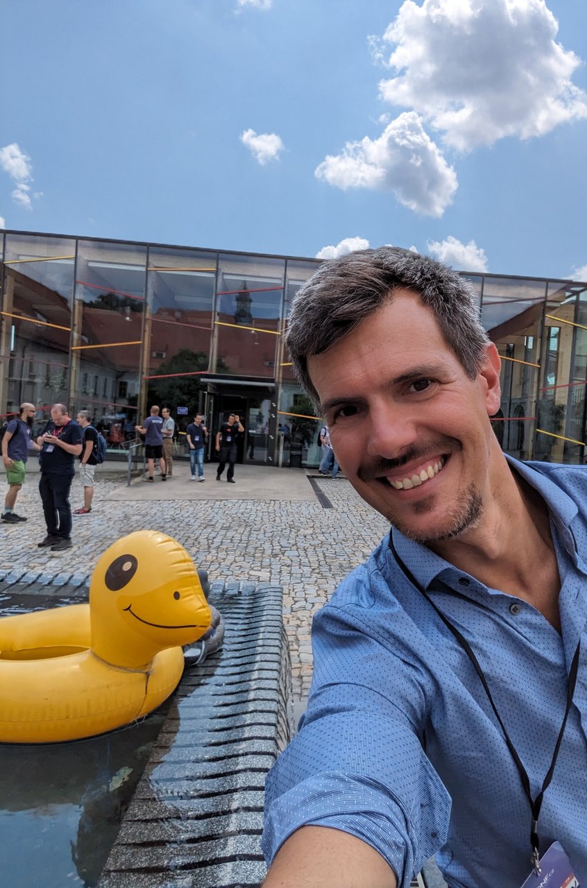 Luca Berton taking a selfie by the giant inflatable rubber duck in the DevConf.cz 2023 courtyard in Brno