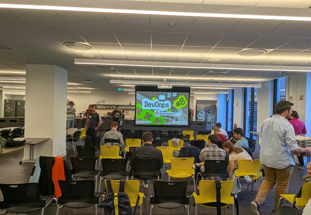 Attendees mingling in the Datadog office before the talks, with the DevOops #8 slide on the screen