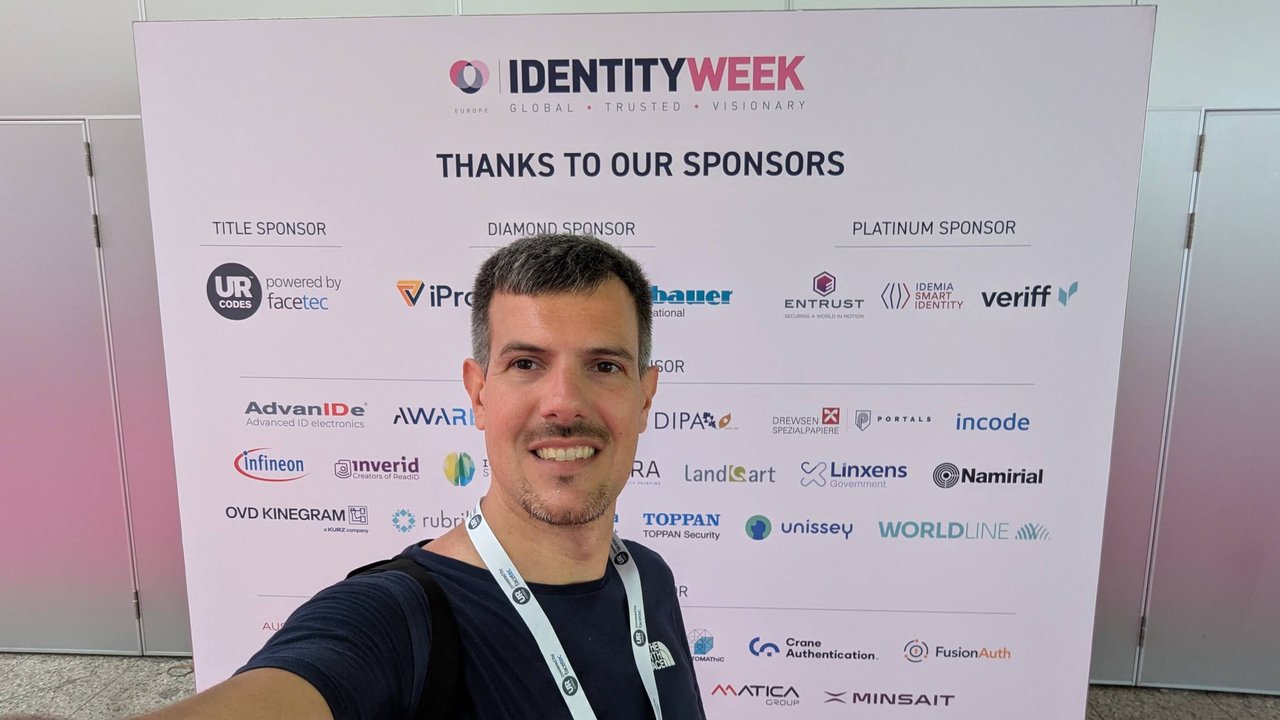 Luca Berton taking a selfie in front of the Identity Week Europe sponsor wall listing title, diamond, platinum and other sponsors