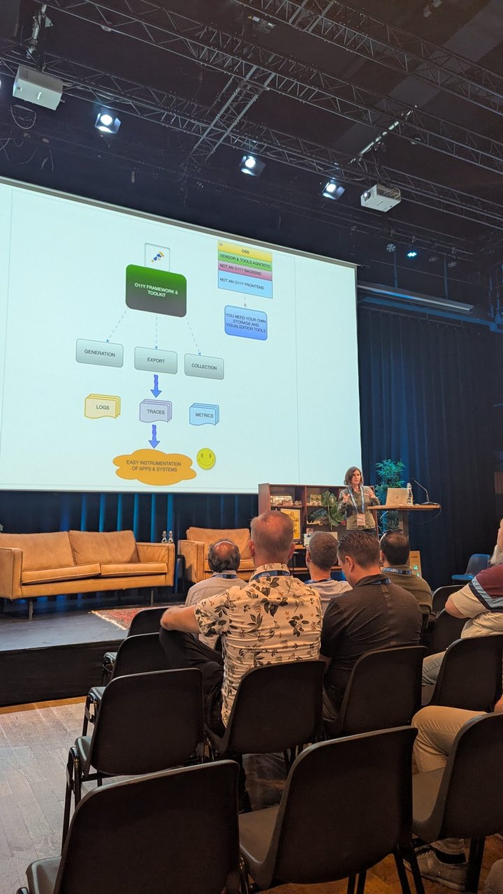 A slide at DevOpsDays Amsterdam showing OpenTelemetry as an observability framework and toolkit for generation, export and collection of logs, traces and metrics, noting it is not a backend or frontend