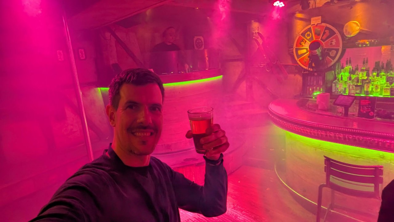 Luca Berton raising a glass in a bar lit in pink and green on the evening of DevWorld 2025