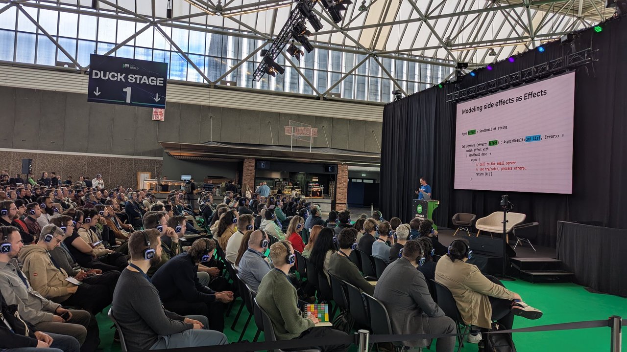 The Duck Stage 1 at DevWorld 2025 with a full audience in wireless headphones and the slide Modeling side effects as Effects