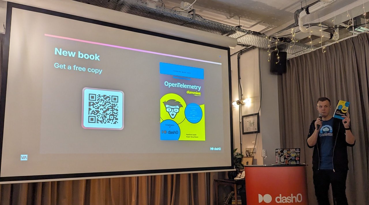 Kasper Borg Nissen holding up a copy of OpenTelemetry For Dummies next to a slide reading New book, Get a free copy, with a QR code and the book cover