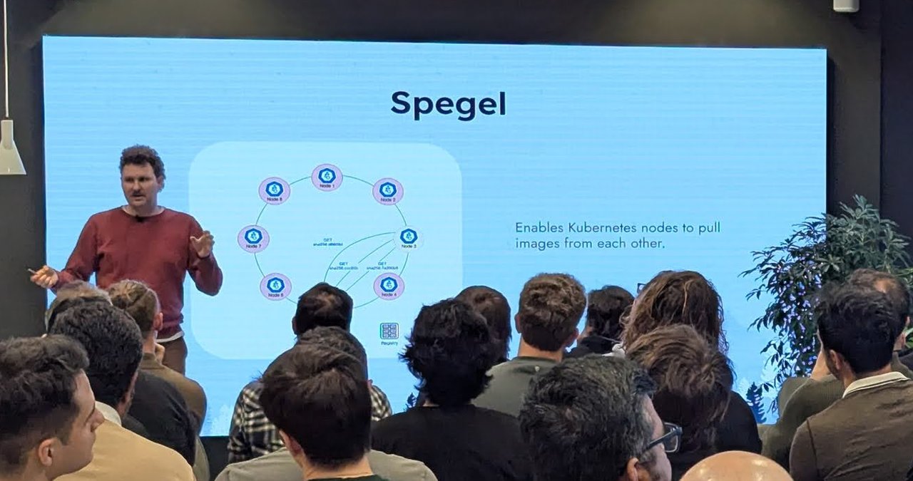 Philip Laine on stage next to the slide Spegel, showing a ring of Kubernetes nodes requesting image layers from each other and the line Enables Kubernetes nodes to pull images from each other