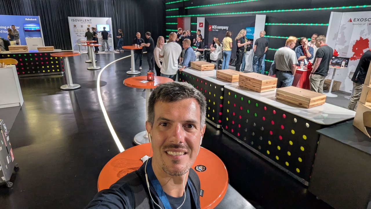 Luca Berton on the expo floor at Dutch Cloud Native Day, with the Isovalent, HCS company and Exoscale booths behind