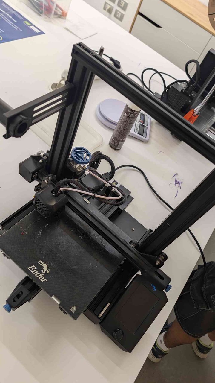 Creality Ender 3 on a white table — dragon logo visible, blue safety sign and second printer in the background