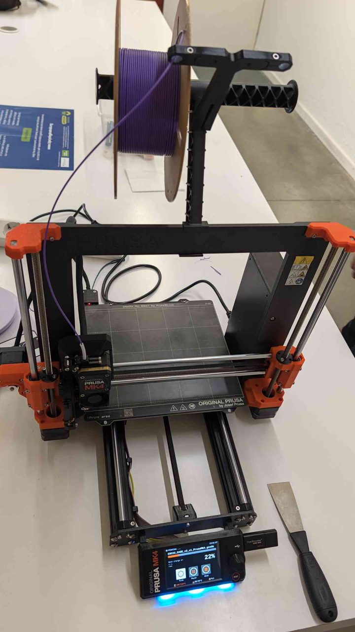 Prusa MK4 close-up — the PEI sheet, orange frame accents, and the USB drive labeled DroiTraveler
