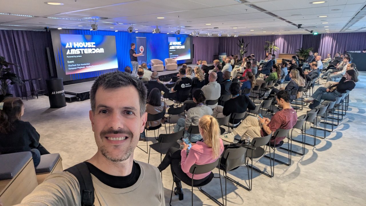 Selfie of Luca Berton in front of the seated audience, with the AI House Amsterdam screen behind the stage