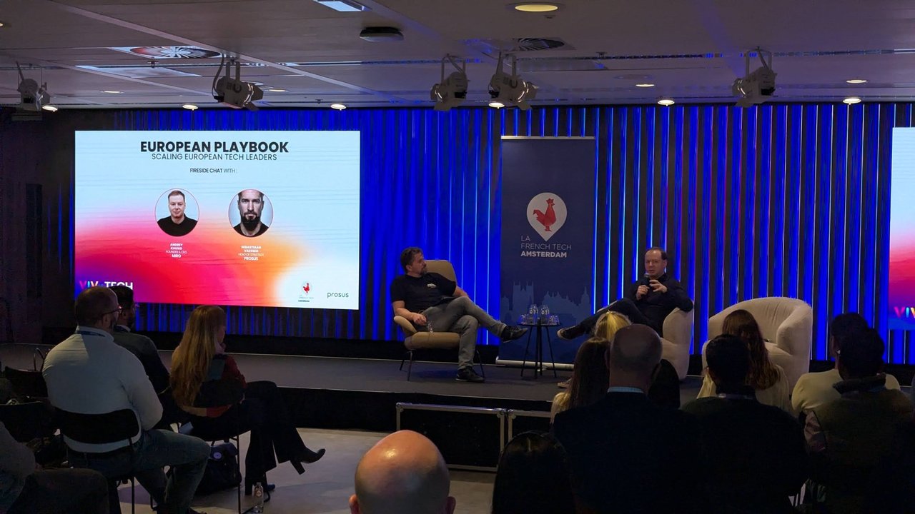 The fireside chat seen from the back of the AI House Amsterdam main hall, with the European Playbook fireside chat slide on screen and the La French Tech Amsterdam banner beside the stage