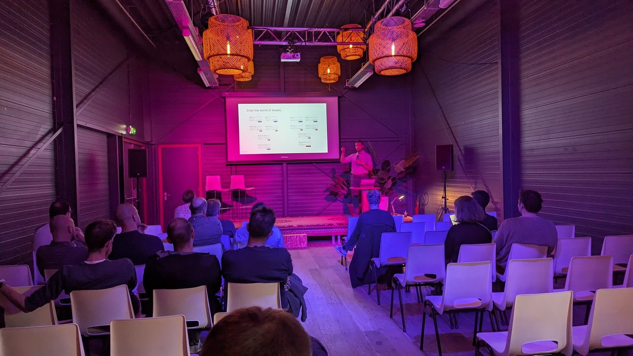 The Overstory speaker on the FikaWorks Day stage presenting a slide titled Enter the world of Assets, showing a Dagster asset graph, to a seated audience