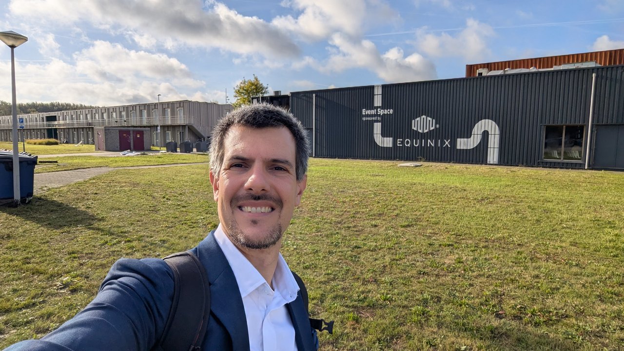 Selfie of Luca Berton on the lawn at Science Park Amsterdam, in front of a dark building with a sign reading Event Space, sponsored by Equinix