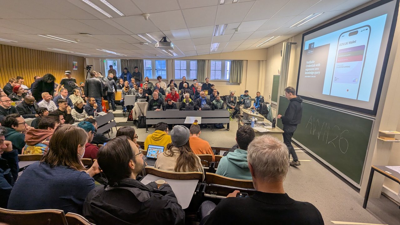 Jesse Wright presenting Verifiable Credentials with expressive zero knowledge query to a full room AW1.126 at FOSDEM 2025, with a GOV.UK Wallet mock-up on screen