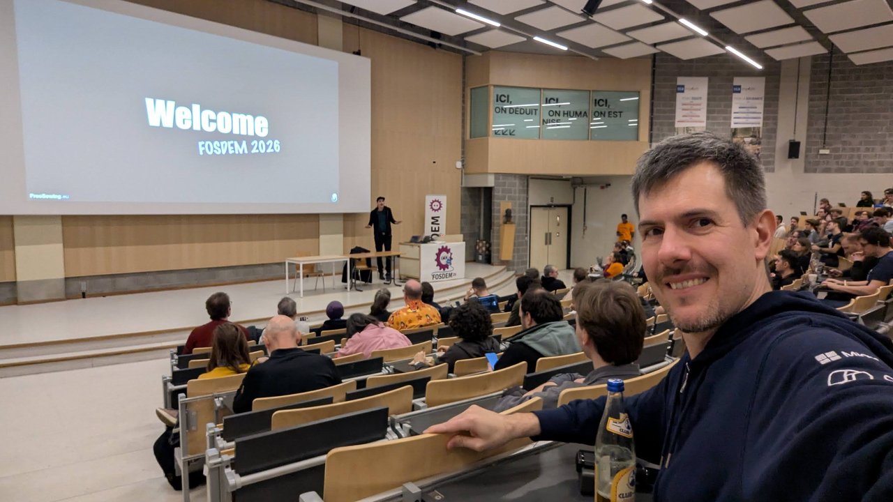 Luca Berton in a large auditorium at ULB Brussels during FOSDEM 2026, with the hall filling up for the next talk