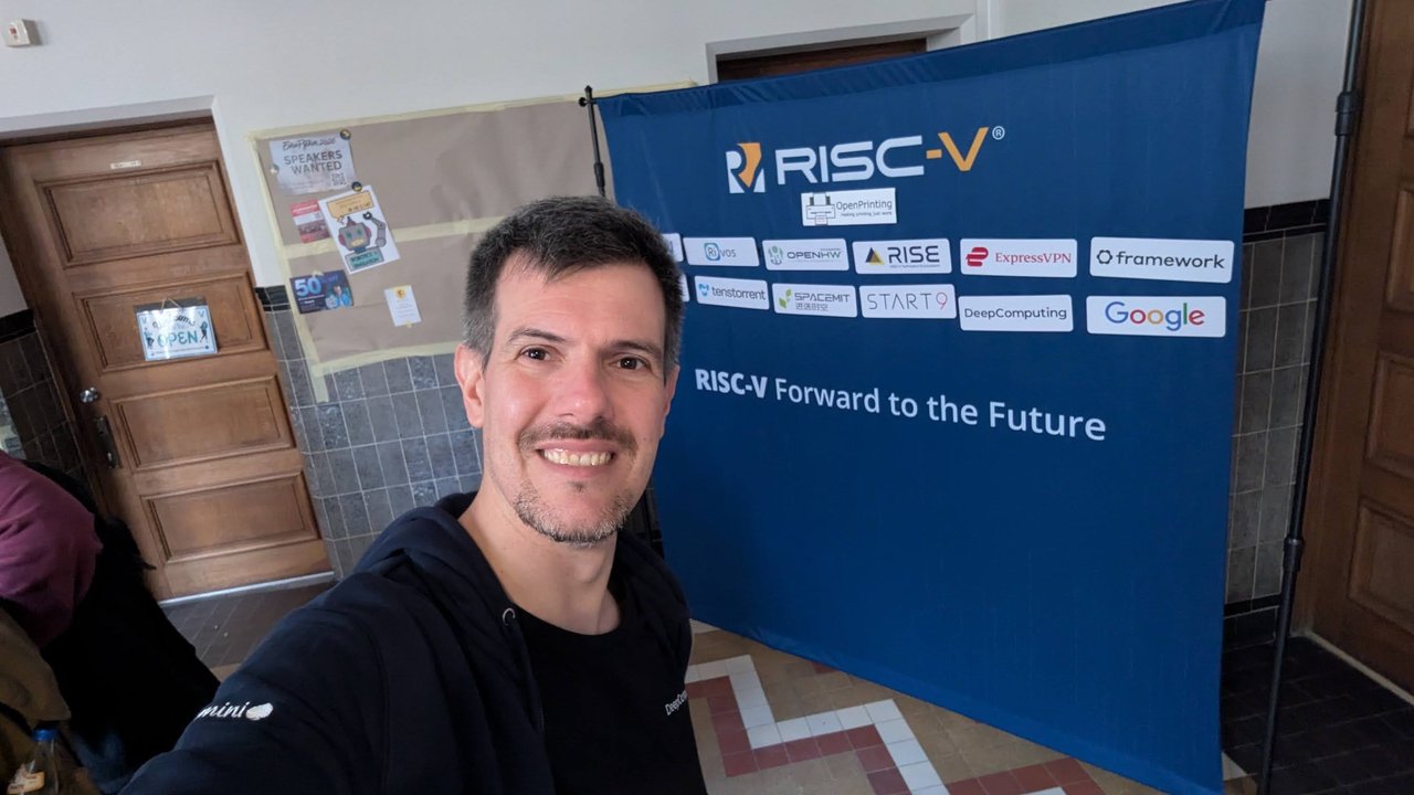 Luca Berton at the RISC-V stand in front of the RISC-V Forward to the Future banner with member logos including RISE, Framework, DeepComputing and Google at FOSDEM 2026