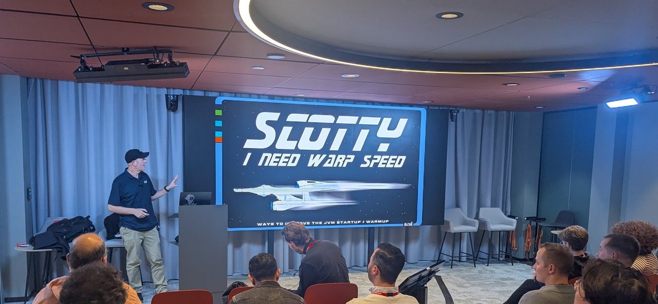 A talk slide reading Scotty I need warp speed with a speaker standing in front of a seated audience