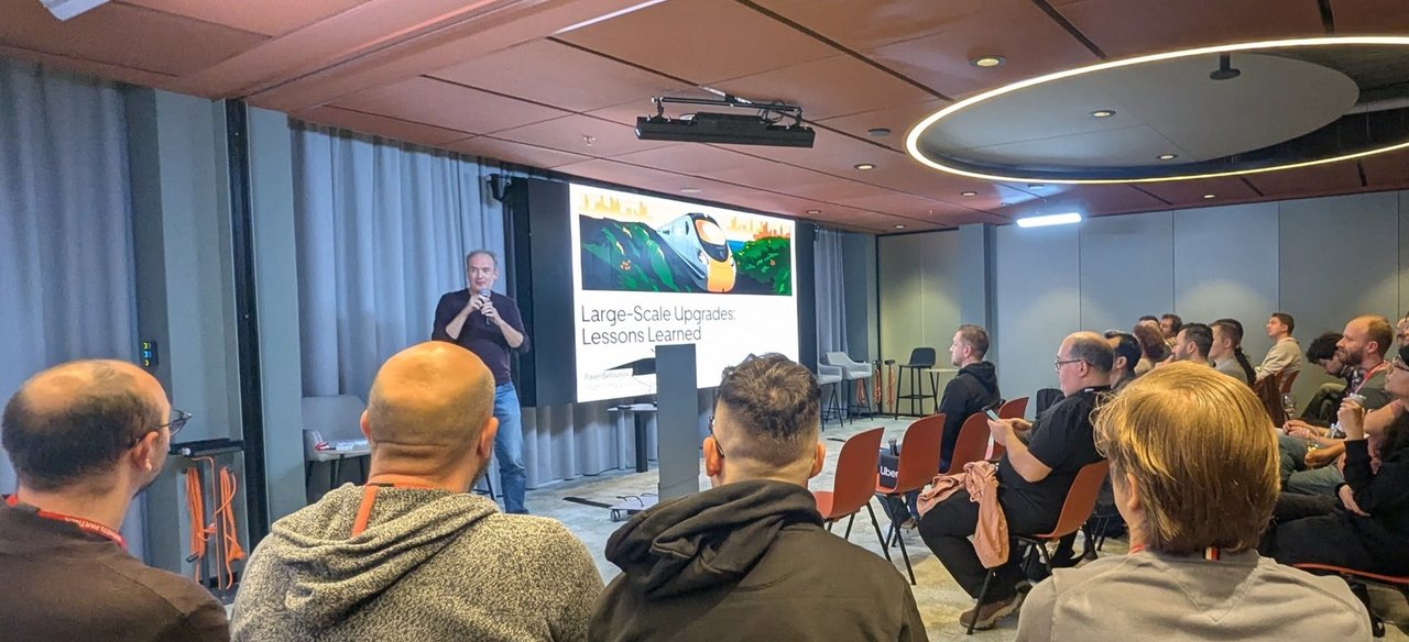 A seated audience at the Friends of OpenJDK meetup at Uber, with the Large-Scale Upgrades title slide on the screen and the speaker holding a microphone