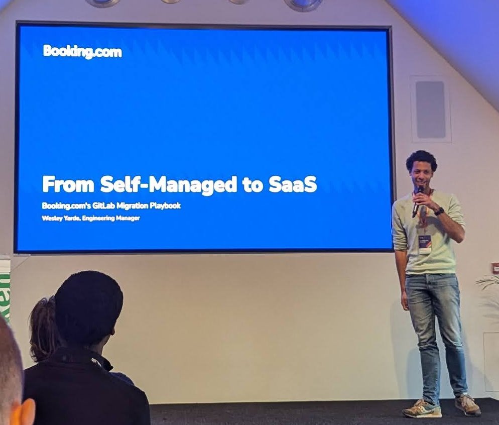 Wesley Yarde on stage next to the Booking.com title slide From Self-Managed to SaaS, Booking.com's GitLab Migration Playbook