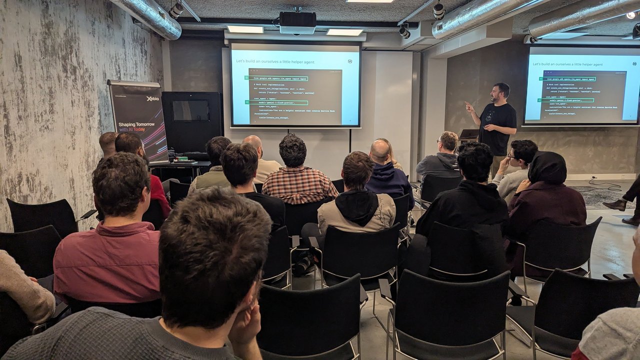 A wide view of the room at the Xebia meetup in Amsterdam while the speaker presents the Let's build an ourselves a little helper agent code slide on two screens