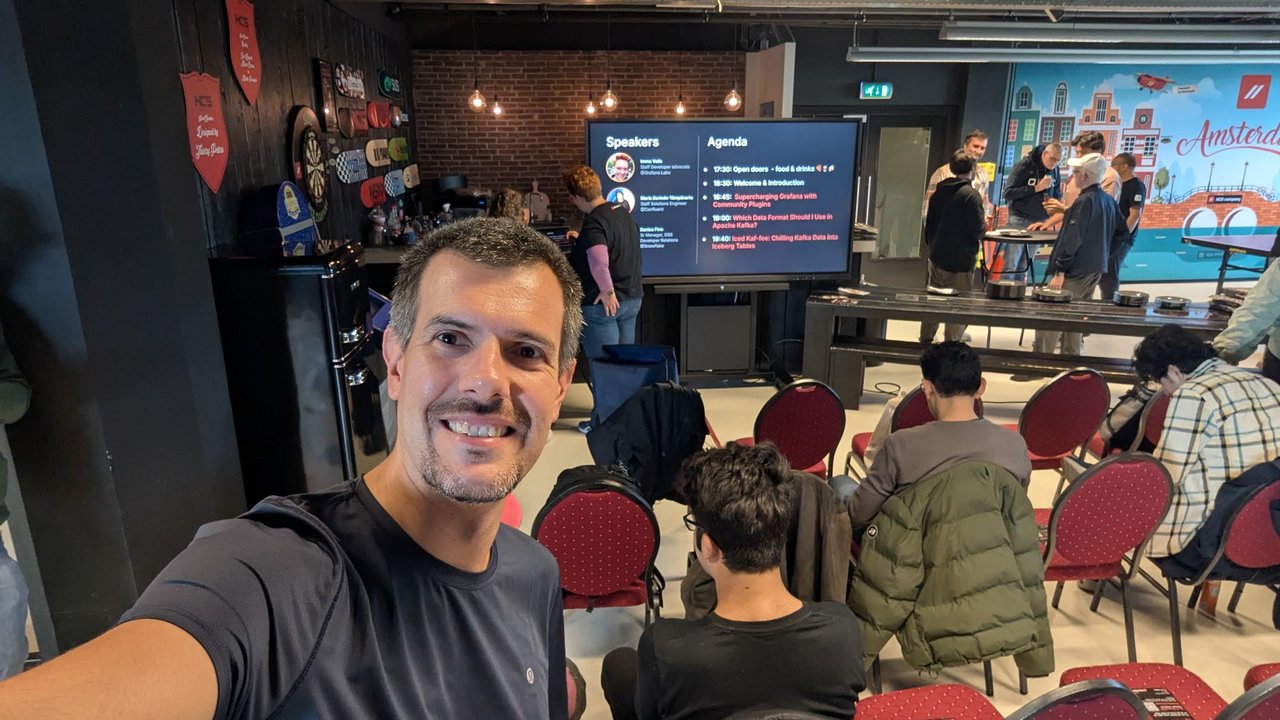 Luca Berton taking a selfie in front of the Speakers and Agenda screen at Grafana & Friends Amsterdam, with attendees arriving behind him