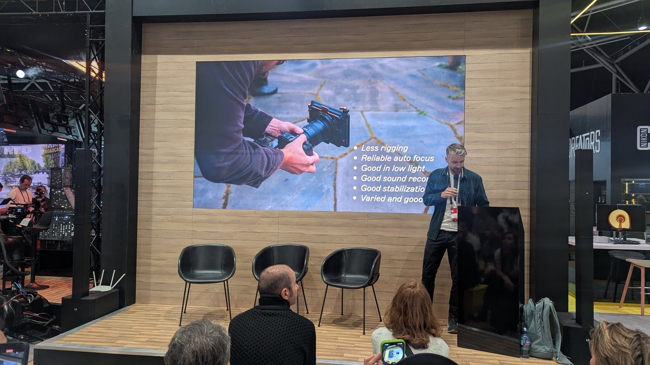 A presenter on the Nikon stand at IBC 2025 next to a slide listing less rigging, reliable auto focus, good in low light, good sound recording and good stabilization