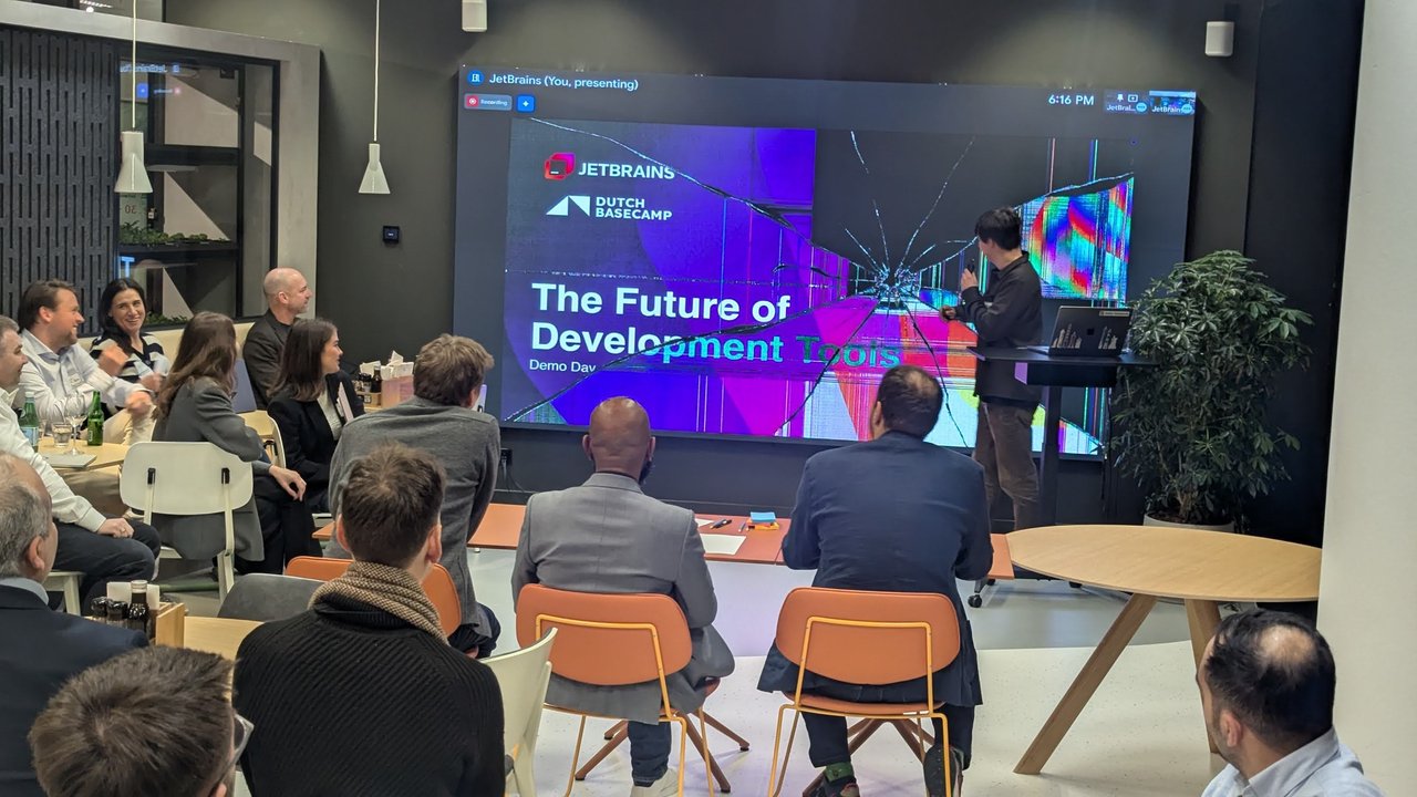 The Future of Development Tools Demo Day title slide with the JetBrains and Dutch Basecamp logos, shown on a large LED wall while the host speaks and the audience sits at tables in front