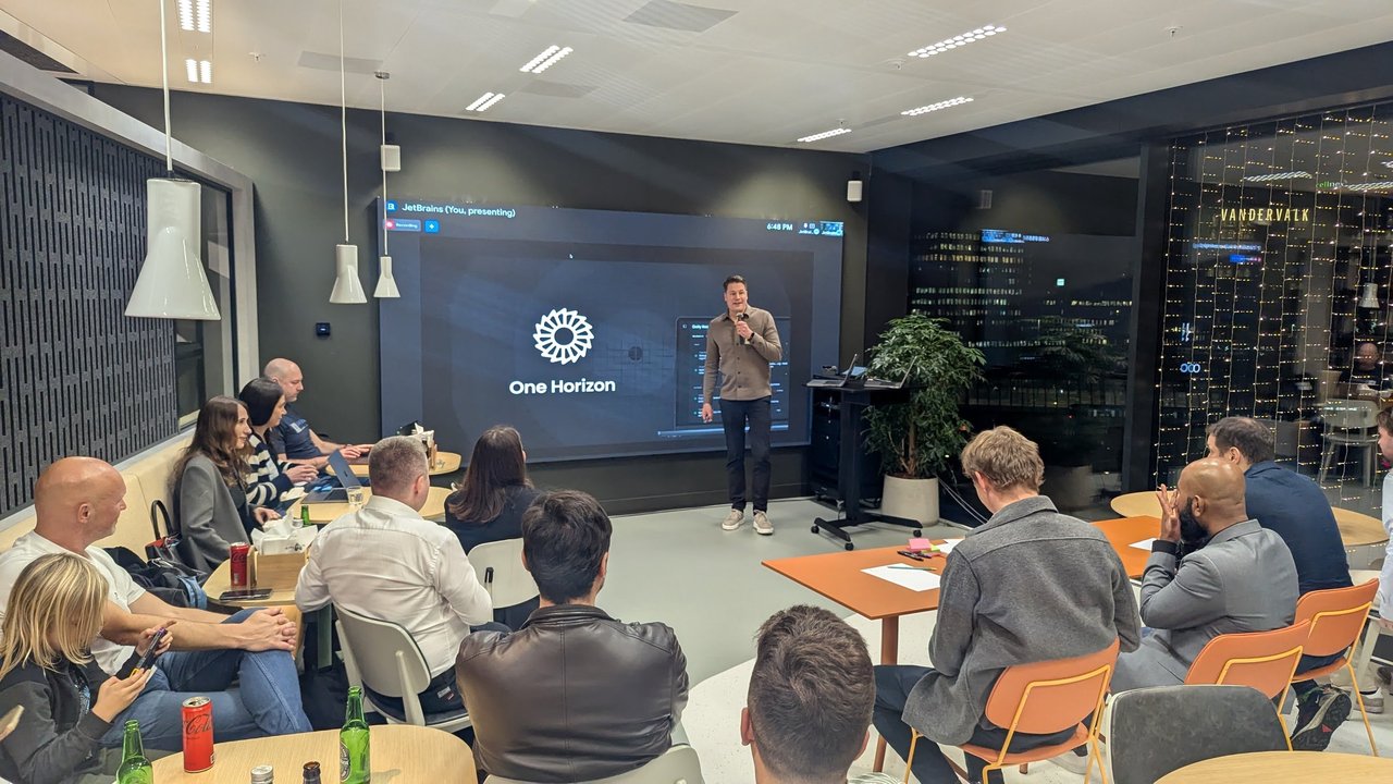 The One Horizon pitch: the logo and a product screenshot on the LED wall, with the founder speaking to the room