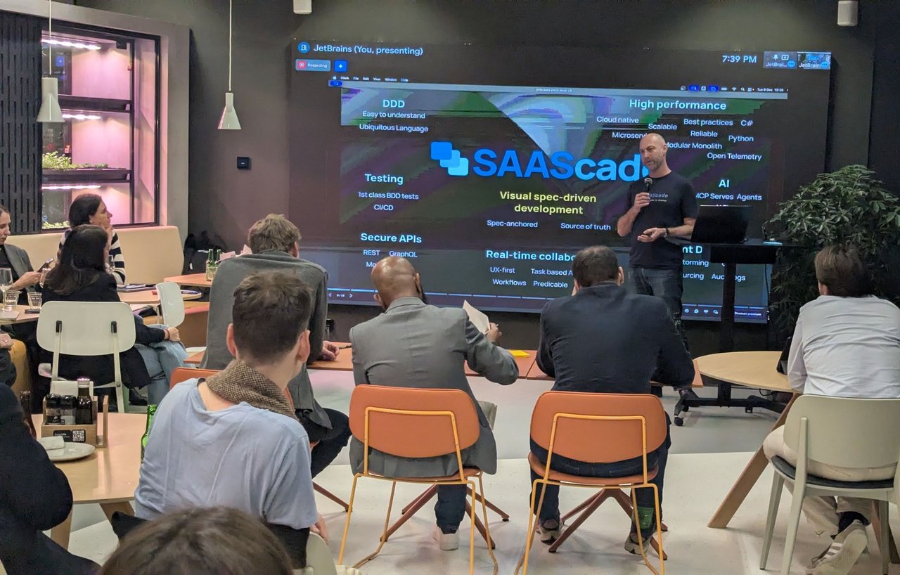 The SAAScade pitch slide: Visual spec-driven development in the centre, surrounded by DDD, Testing, Secure APIs, Real-time collaboration, High performance and AI, with the speaker in front of the judges