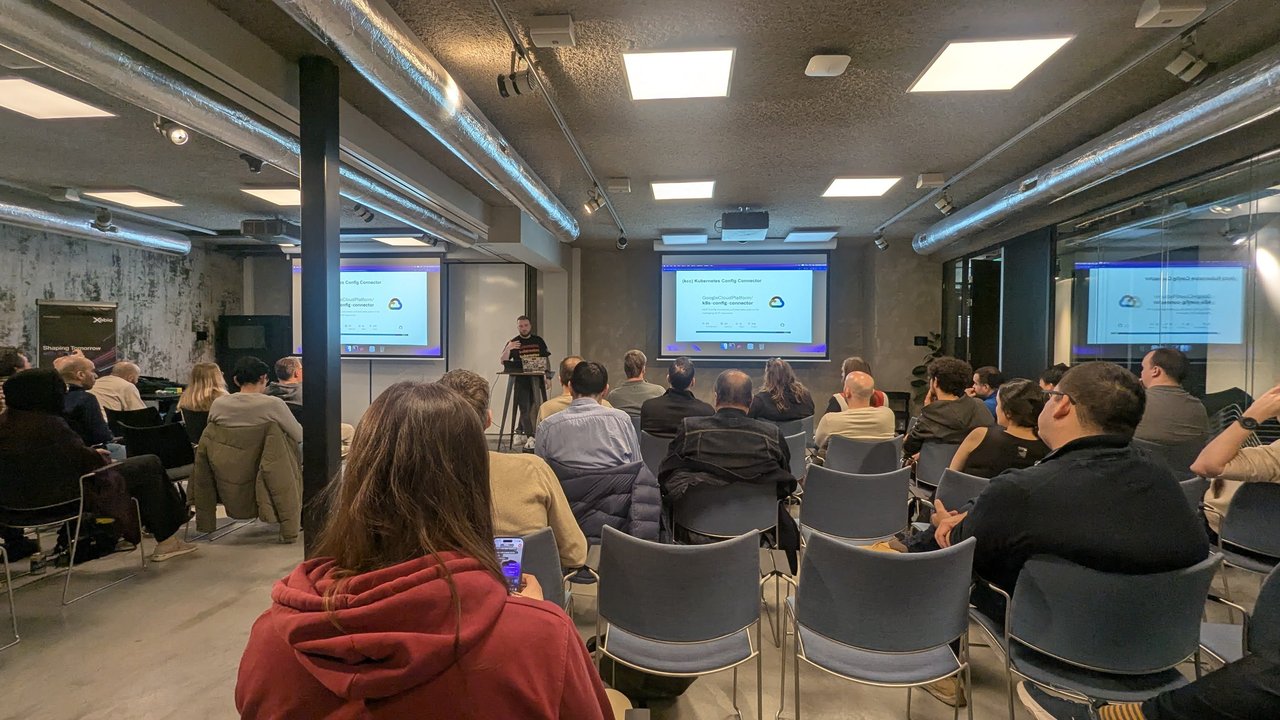 Wide view of the room at the Xebia meetup in Amsterdam with the speaker presenting the (kcc) Kubernetes Config Connector slide on several screens