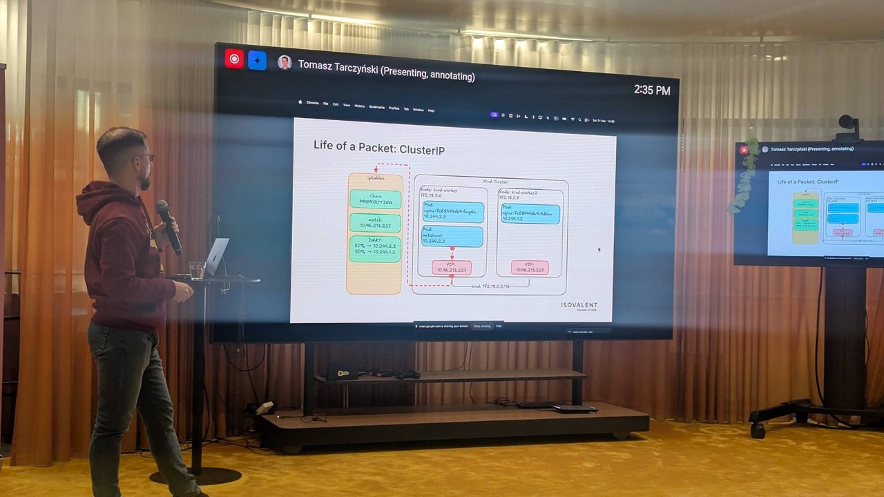 Tomasz Tarczyński presenting a Life of a Packet: ClusterIP slide with an iptables DNAT box and a two-worker kind cluster at Cloud Native Rejekts 2026