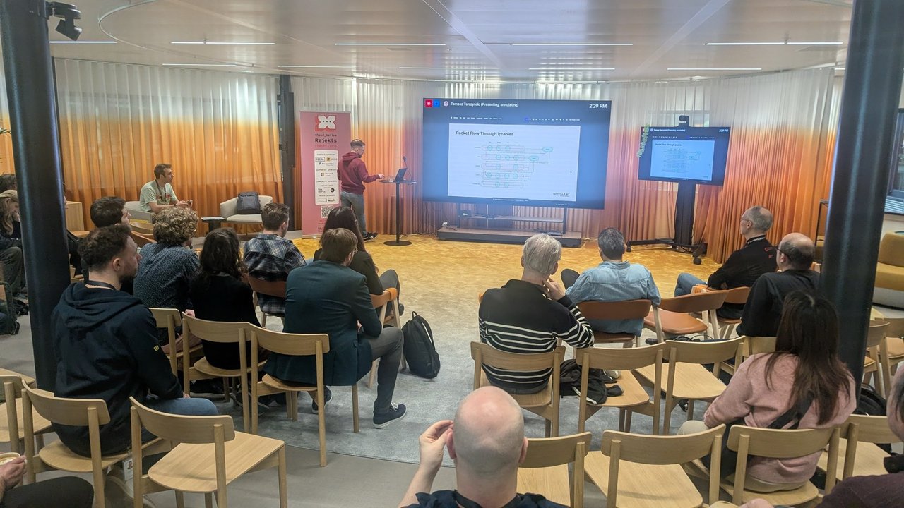 Tomasz TarczyĹski presenting a Packet Flow Through iptables diagram of netfilter tables and chains to the audience in Room 2 at Cloud Native Rejekts 2026