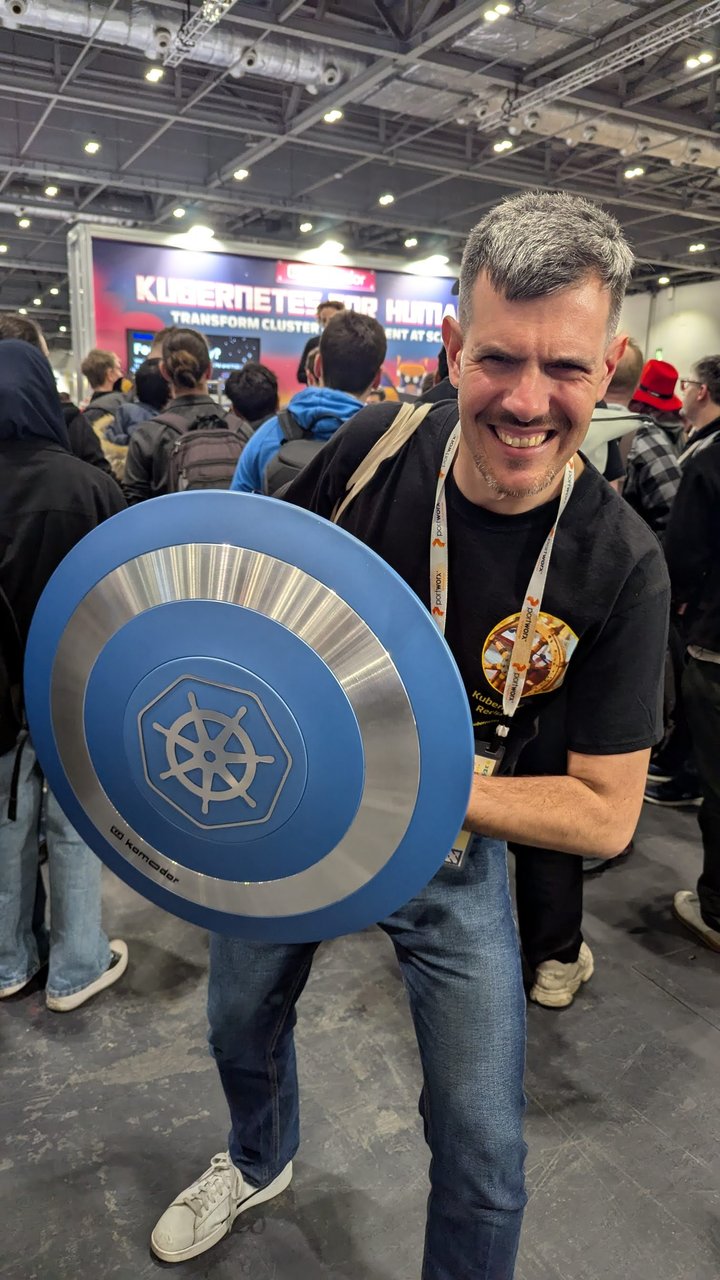 Luca Berton holding a blue Kubernetes shield on the expo floor at KubeCon Europe 2025