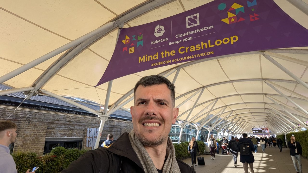 Luca Berton taking a selfie under a purple Mind the CrashLoop KubeCon CloudNativeCon Europe 2025 banner on the walkway to the venue