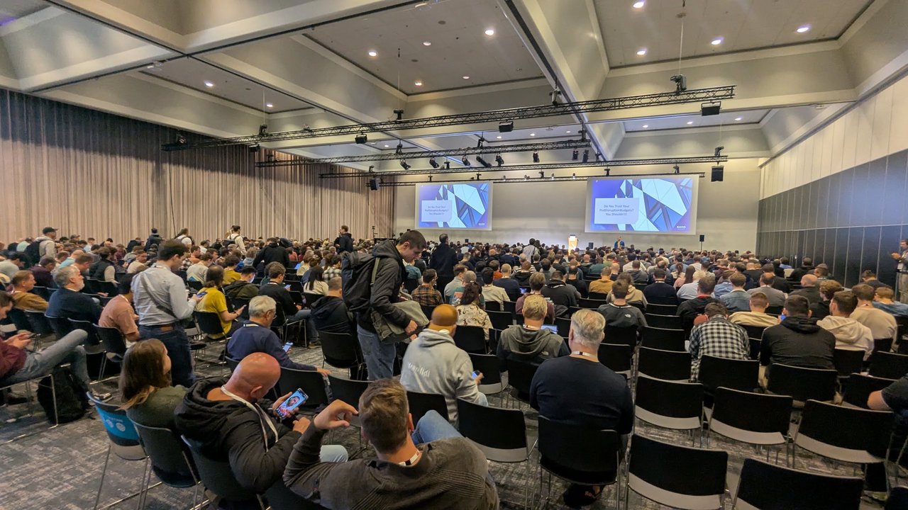 A large breakout room at KubeCon Europe 2026 filling up for a Saxo session titled Do You Trust Your PodDisruptionBudgets? You Shouldn't!