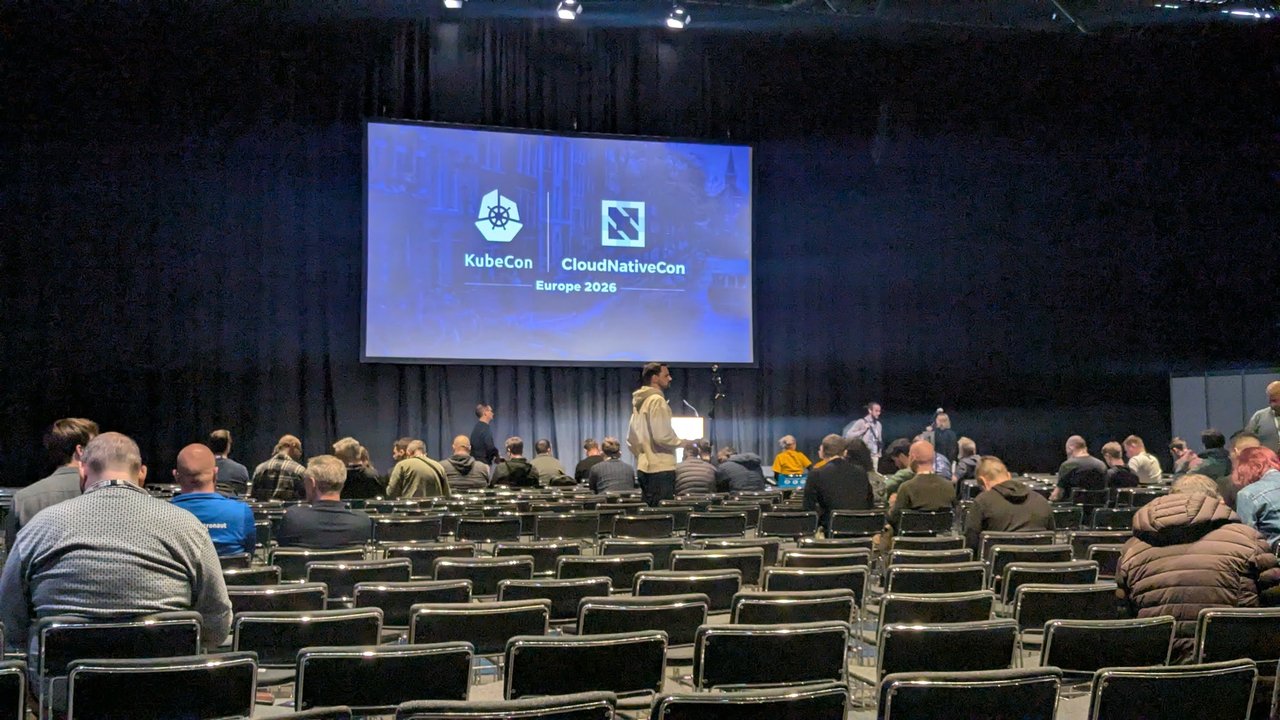 The KubeCon + CloudNativeCon Europe 2026 logo on a large screen above rows of seats on Monday evening