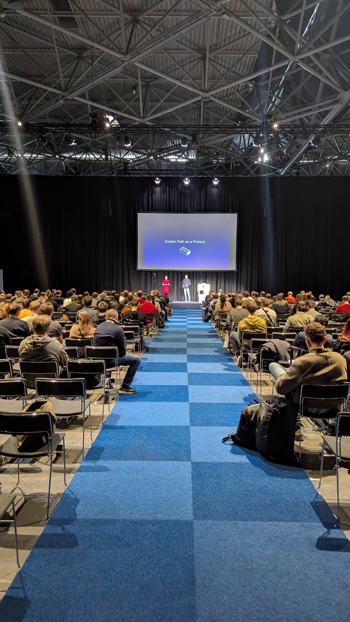 The Platform Engineering Day Europe hall at RAI Amsterdam, with a long blue carpet aisle leading to the stage and a full audience on both sides