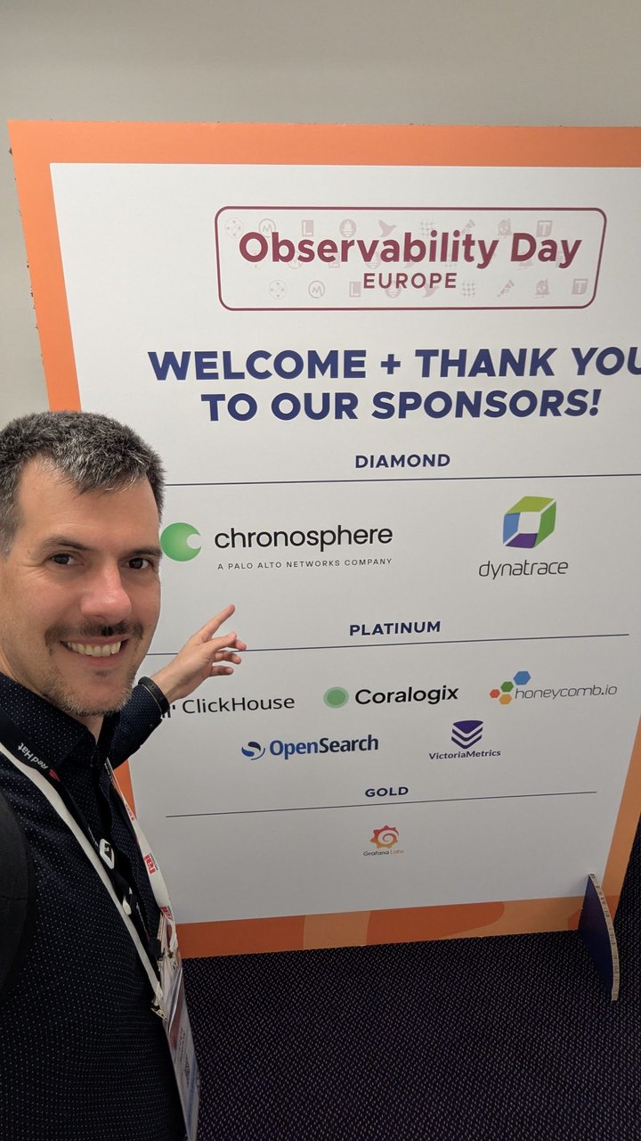 Luca Berton pointing at the sponsor board for Observability Day Europe 2026 at KubeCon Amsterdam