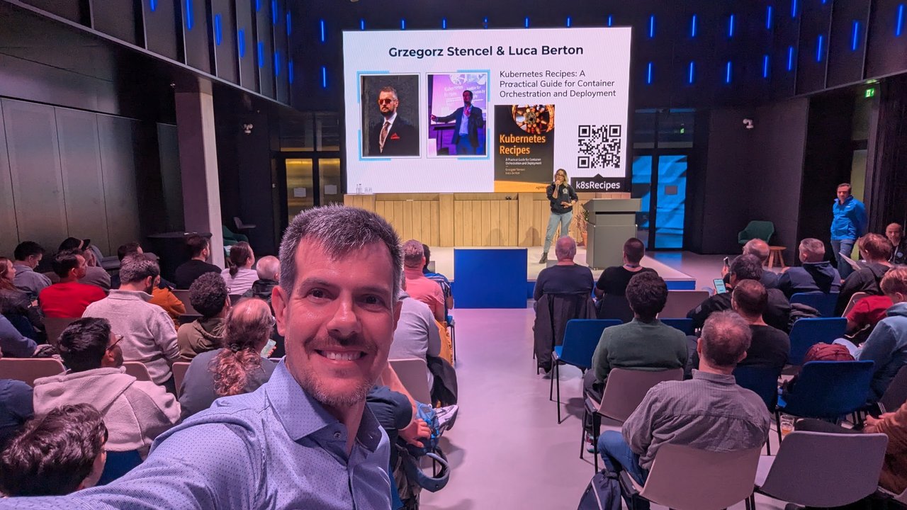 Luca Berton at Signal Overflow at Booking.com HQ in Amsterdam, with a slide reading Grzegorz Stencel and Luca Berton, Kubernetes Recipes, behind him