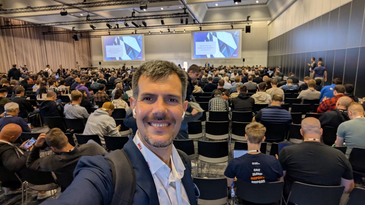A selfie in a large breakout room at KubeCon Europe 2026 filling up before the session Do You Trust Your PodDisruptionBudgets? You Shouldn't!, with the title slide on both screens