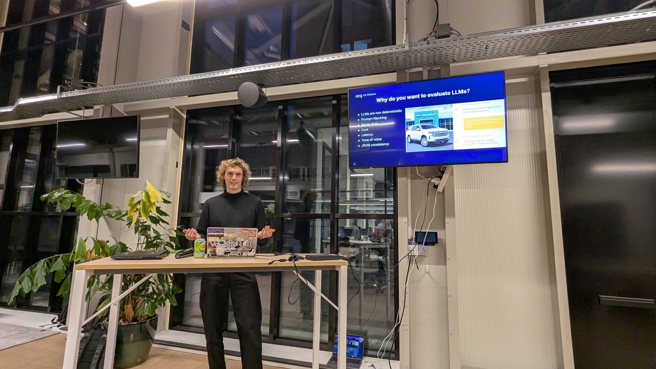 Cormick Marskamp presenting the orq.ai slide Why do you want to evaluate LLMs at AI Tinkerers Amsterdam, listing non-determinism, prompt hijacking, cost, latency, tone of voice and JSON consistency