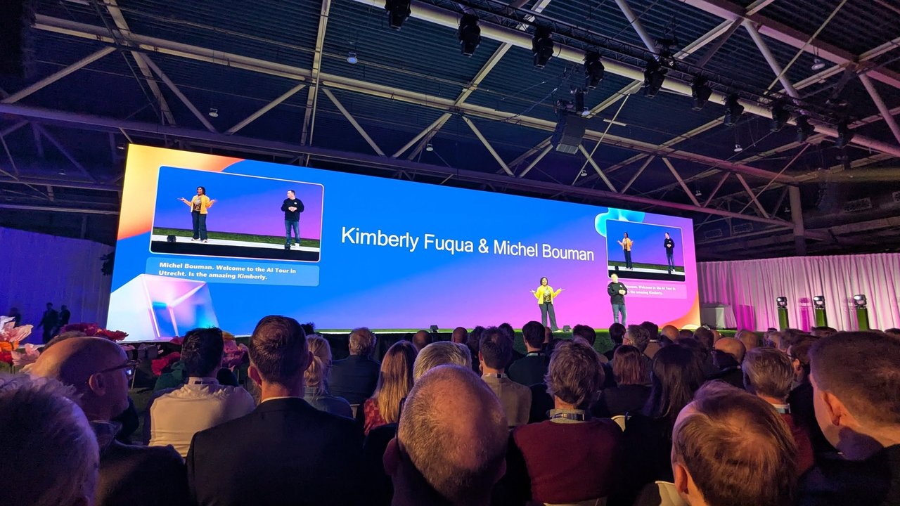 Two presenters on the keynote stage at the Microsoft AI Tour in Utrecht, with their names Kimberly Fuqua and Michel Bouman on the big screen and the audience in front