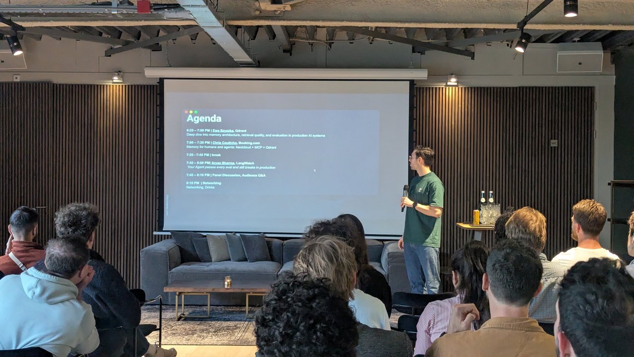 The Agenda slide for the MLOps Community Amsterdam evening, with a presenter holding a microphone next to the screen