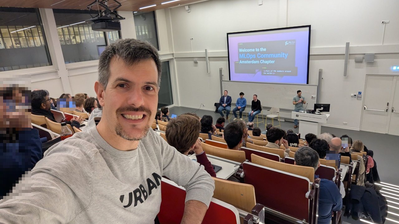 Luca Berton in the Universiteit van Amsterdam lecture hall with the Welcome to the MLOps Community Amsterdam Chapter slide and the panel on stage behind him