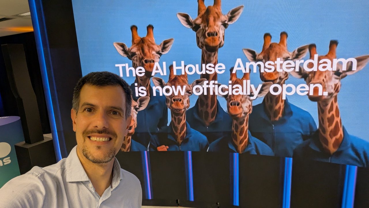 Selfie of Luca Berton in front of the AI House screen reading The AI House Amsterdam is now officially open, with a group of giraffes in blue tracksuits