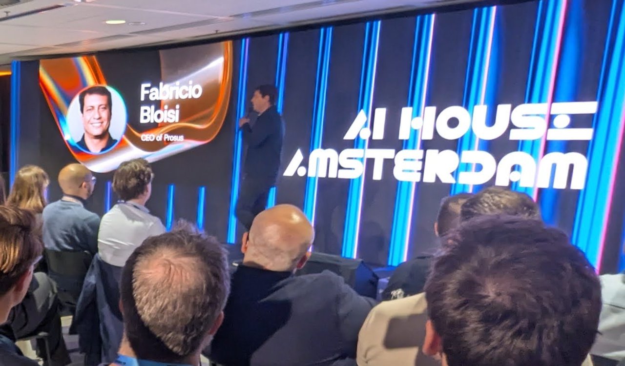 AI House Amsterdam main hall with Fabricio Bloisi, CEO of Prosus, on the screen next to the AI House Amsterdam logo and a speaker on stage