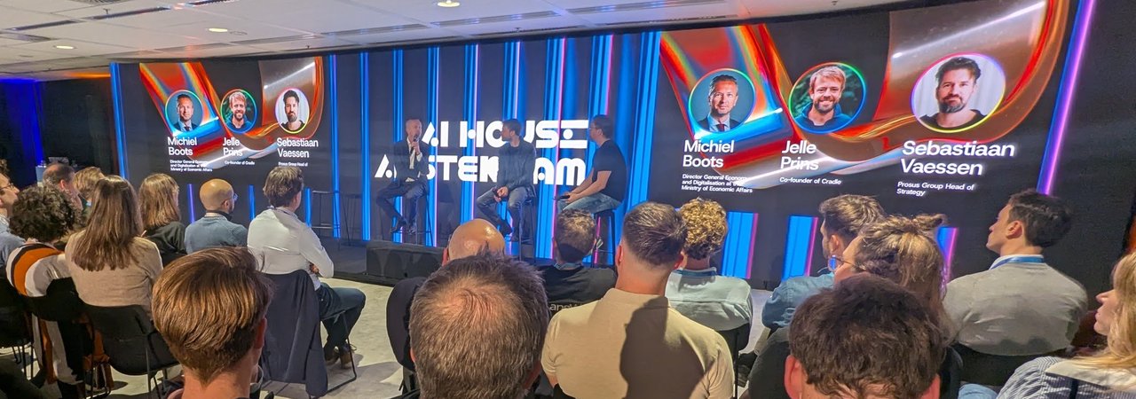 AI House Amsterdam stage with the first panel and screens naming Michiel Boots of the Ministry of Economic Affairs, Jelle Prins of Cradle and Sebastiaan Vaessen of Prosus