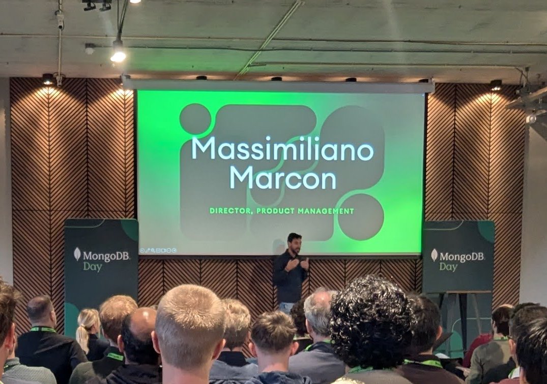 MongoDB Day Amsterdam 2025 keynote room with a green title slide reading Massimiliano Marcon, Director, Product Management, a speaker on stage and two MongoDB Day banners