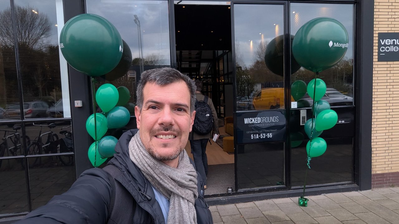 Selfie of Luca Berton at the entrance of Venue Collective for MongoDB Day Amsterdam 2025, with green MongoDB balloons on both sides of the door