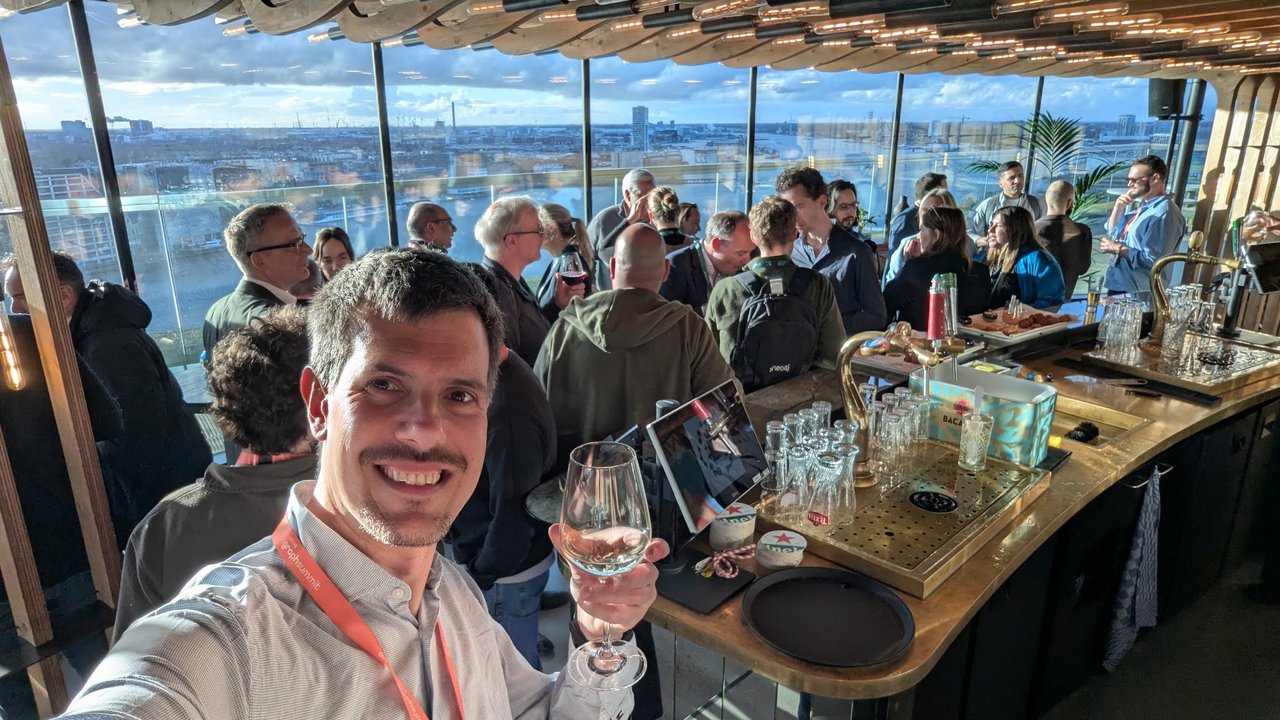 Luca Berton at the GraphSummit Amsterdam 2025 networking drinks in A'DAM Tower with attendees and the city skyline behind