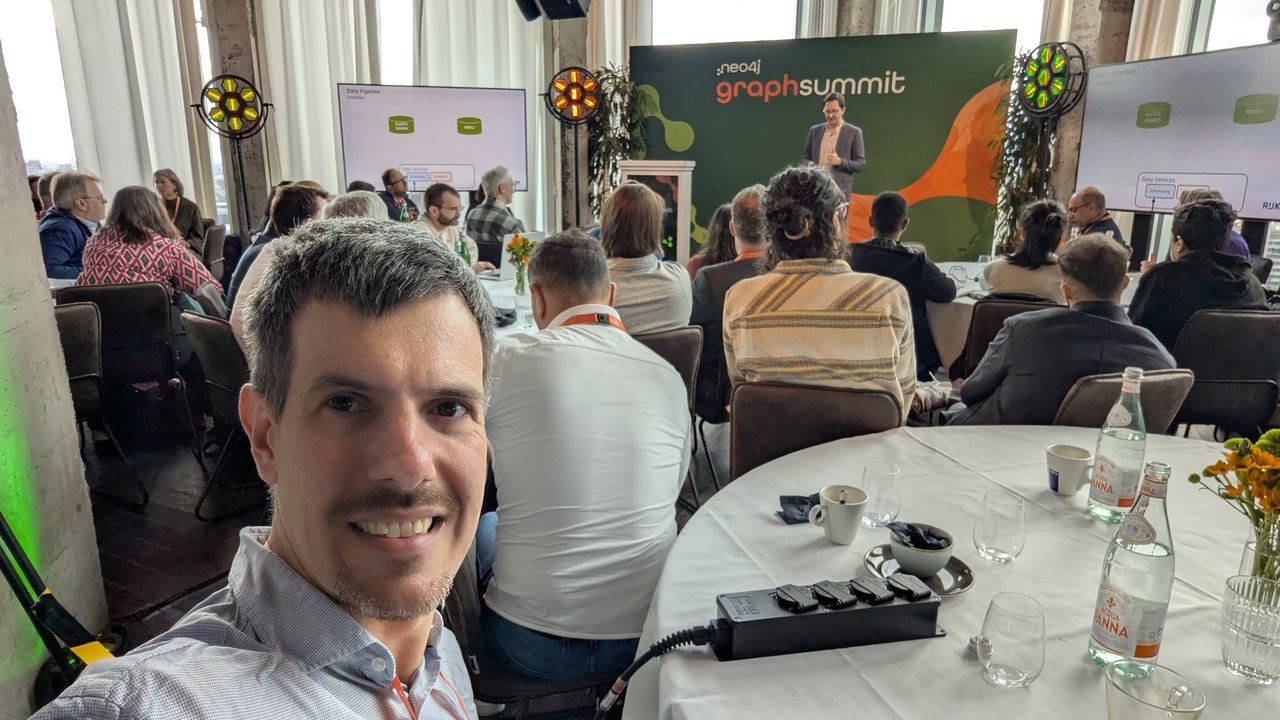 Luca Berton at a table at Neo4j GraphSummit Amsterdam 2025 with the GraphSummit stage and audience behind him